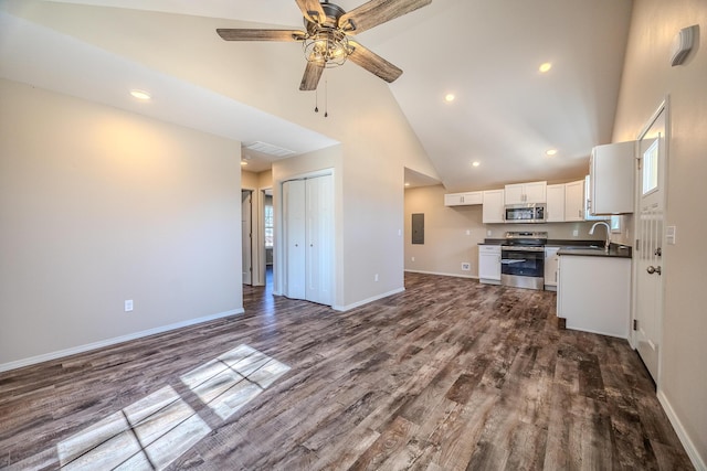 kitchen with white cabinets, dark countertops, appliances with stainless steel finishes, open floor plan, and wood finished floors