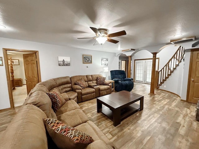 living area with arched walkways, stairway, a ceiling fan, light wood-type flooring, and ornate columns