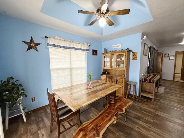 dining space featuring ceiling fan, baseboards, a raised ceiling, and dark wood-type flooring