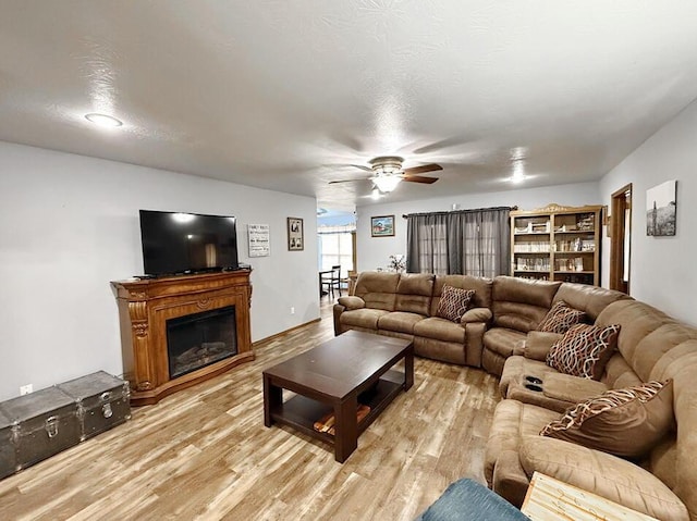 living area featuring light wood-type flooring, a glass covered fireplace, ceiling fan, and a textured ceiling