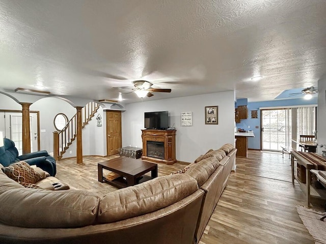 living area featuring ceiling fan, arched walkways, a fireplace, wood finished floors, and decorative columns