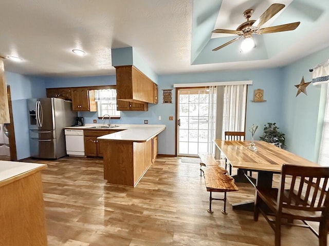 kitchen featuring brown cabinets, a raised ceiling, light countertops, white dishwasher, and a peninsula