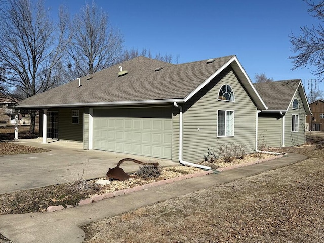 view of side of home featuring a garage, a shingled roof, and concrete driveway