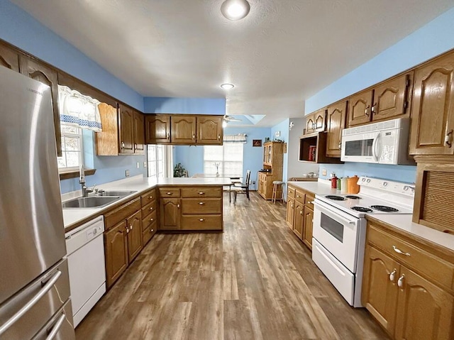 kitchen with white appliances, brown cabinets, a peninsula, light countertops, and a sink