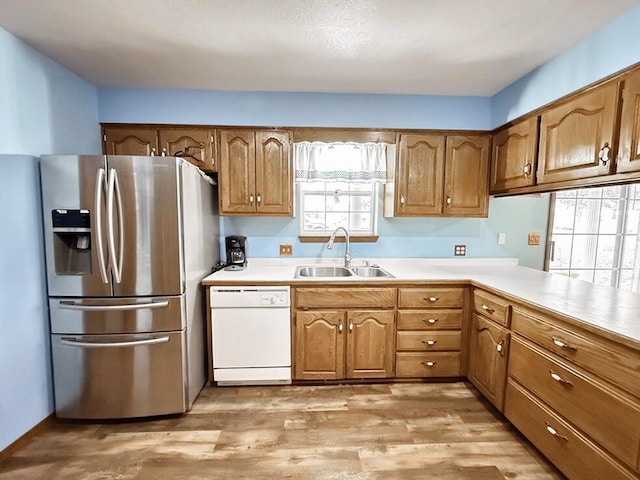 kitchen featuring a sink, light countertops, dishwasher, brown cabinetry, and stainless steel fridge