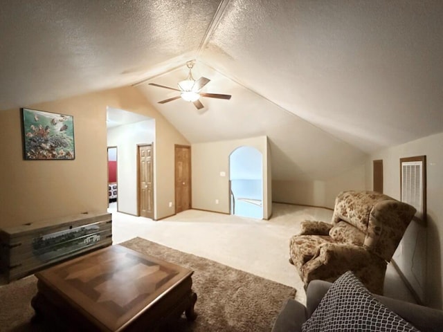 living area featuring a ceiling fan, lofted ceiling, light colored carpet, and a textured ceiling