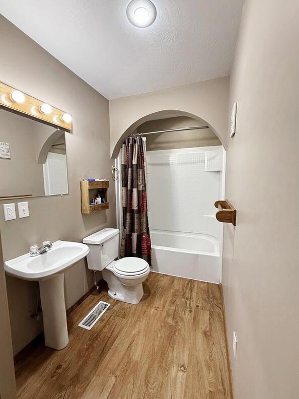 bathroom featuring a textured ceiling, toilet, wood finished floors, visible vents, and shower / bath combination with curtain