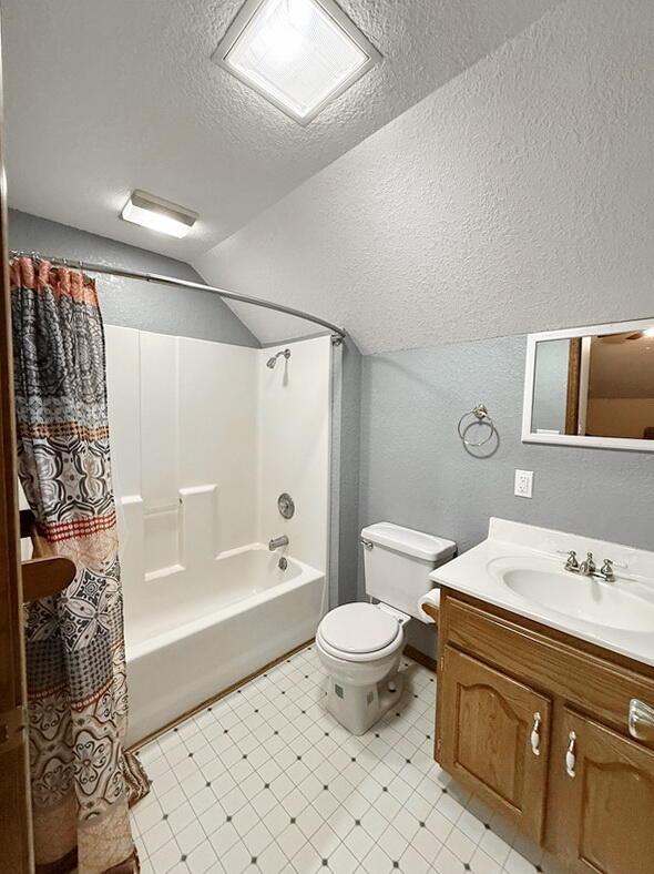 full bathroom featuring a textured ceiling, a textured wall, visible vents, vaulted ceiling, and shower / bath combo