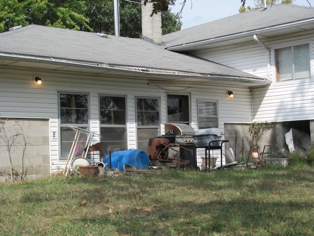 rear view of house with a shingled roof, a chimney, and a lawn