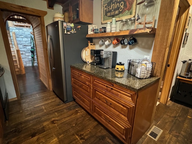 kitchen with visible vents, glass insert cabinets, freestanding refrigerator, dark wood-type flooring, and dark stone counters