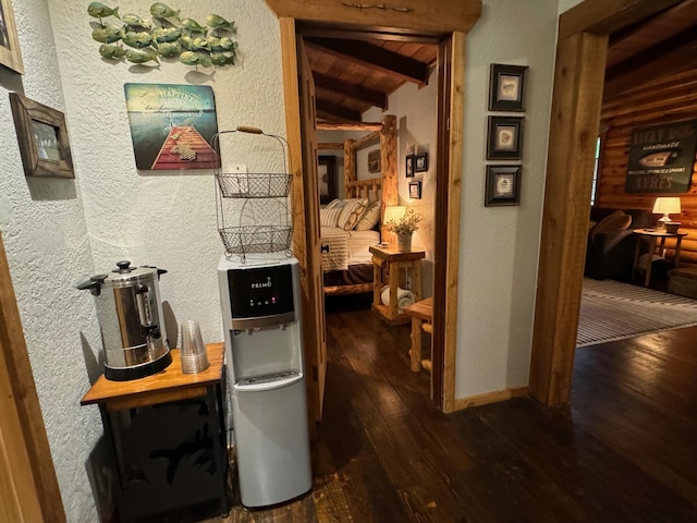 hallway featuring vaulted ceiling with beams, dark wood-style floors, baseboards, and a textured wall