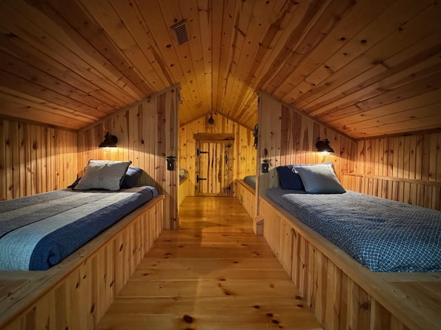 bedroom featuring lofted ceiling, light wood finished floors, wooden walls, and visible vents