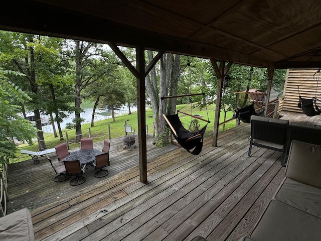 wooden deck with outdoor dining space, a water view, and a yard