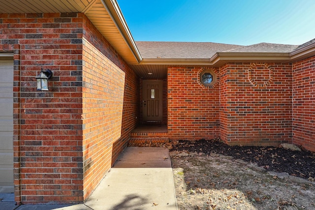 property entrance featuring a shingled roof and brick siding