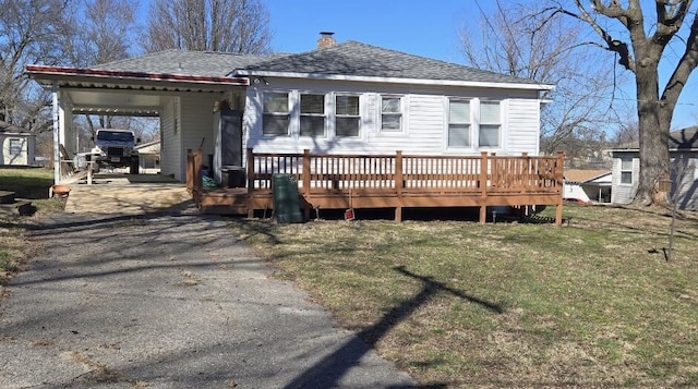 view of front of house with a deck, aphalt driveway, an attached carport, roof with shingles, and a front lawn