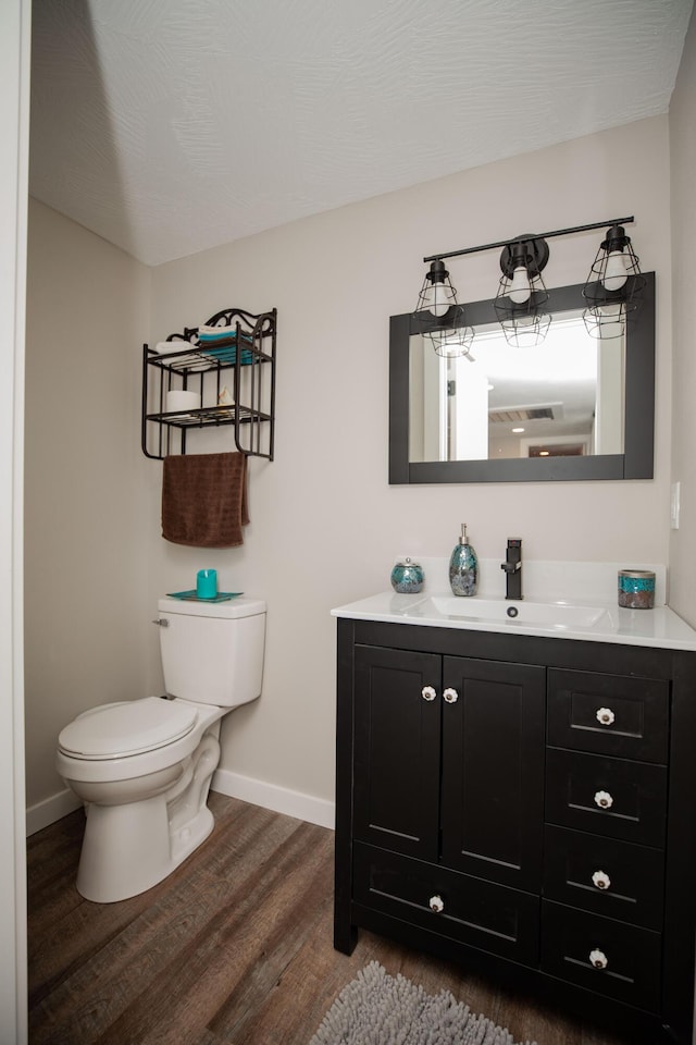 half bathroom with toilet, wood finished floors, vanity, and baseboards