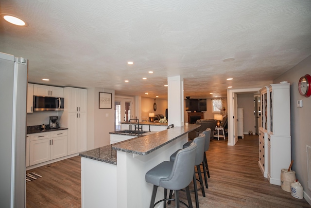 kitchen featuring dark wood finished floors, stainless steel microwave, a kitchen bar, white cabinetry, and a sink