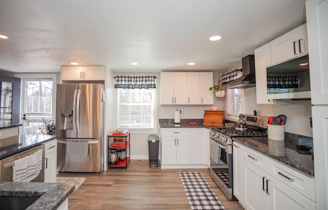 kitchen featuring appliances with stainless steel finishes, dark stone countertops, white cabinetry, and wall chimney exhaust hood