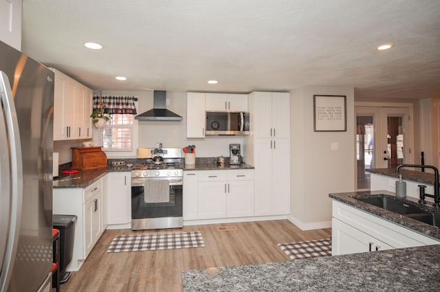 kitchen featuring wall chimney range hood, white cabinetry, stainless steel appliances, and a sink