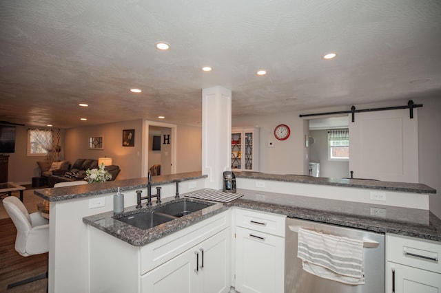 kitchen featuring stainless steel dishwasher, a barn door, open floor plan, white cabinets, and a peninsula