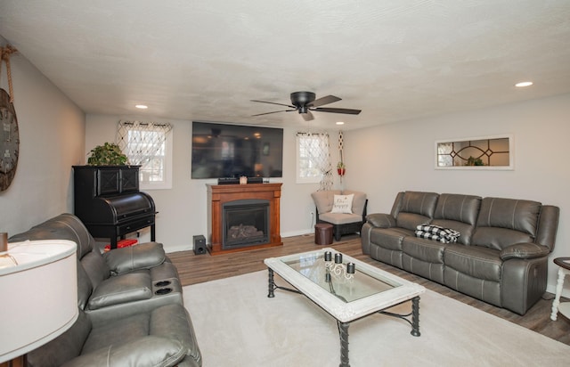 living room featuring recessed lighting, a ceiling fan, a glass covered fireplace, wood finished floors, and baseboards