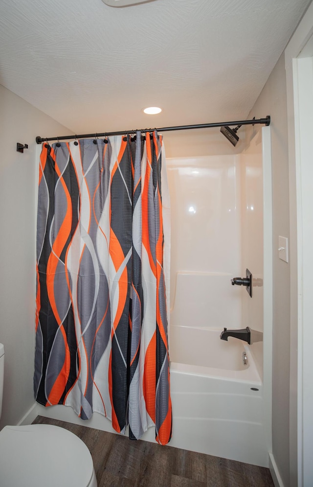 bathroom with toilet, a textured ceiling, shower / tub combo with curtain, and wood finished floors