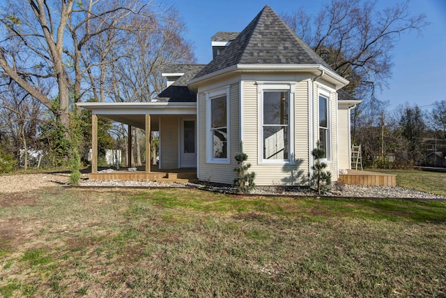 view of side of home with covered porch, a shingled roof, and a lawn