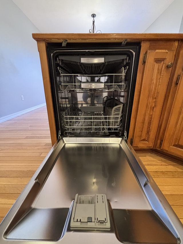 room details with dishwashing machine, brown cabinetry, wood finished floors, and baseboards