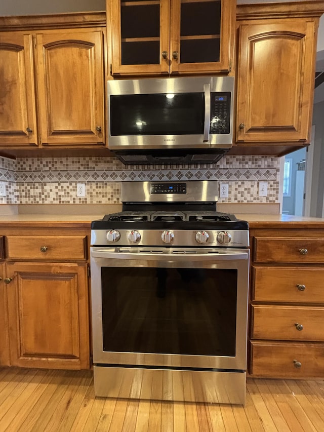 kitchen with appliances with stainless steel finishes, brown cabinets, light countertops, and glass insert cabinets