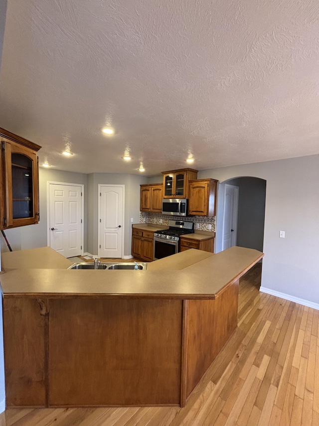 kitchen featuring arched walkways, appliances with stainless steel finishes, brown cabinetry, glass insert cabinets, and a sink