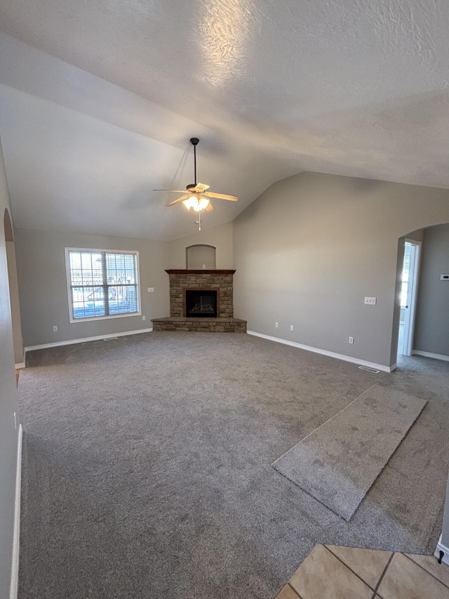 unfurnished living room with arched walkways, carpet, lofted ceiling, a fireplace with raised hearth, and ceiling fan