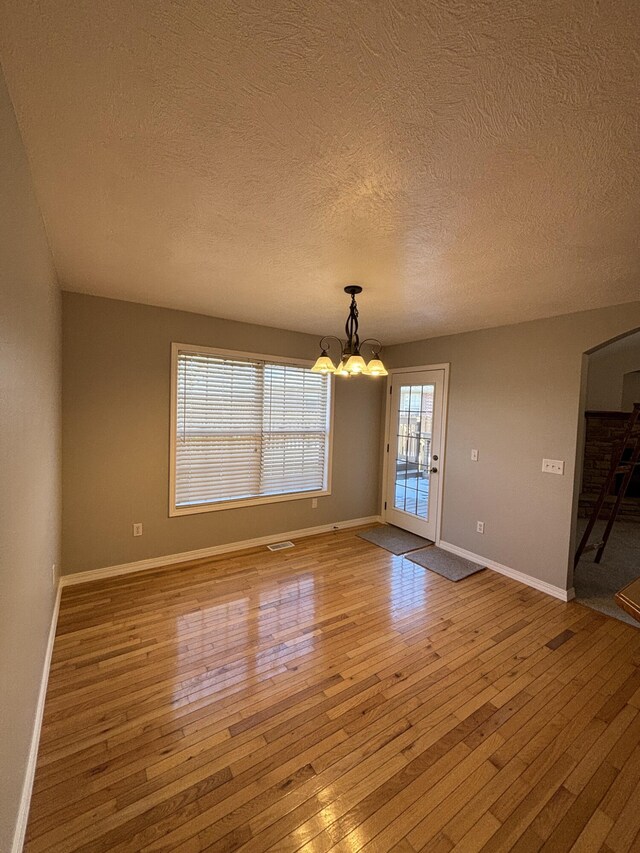 unfurnished dining area featuring visible vents, baseboards, wood-type flooring, an inviting chandelier, and a textured ceiling