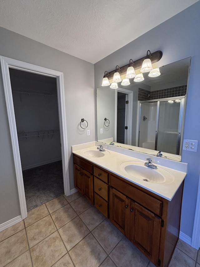 bathroom with double vanity, a shower stall, a textured ceiling, and a sink