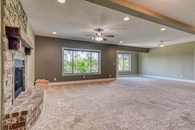 unfurnished living room with carpet floors, a stone fireplace, baseboards, and a textured ceiling