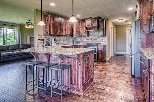 kitchen featuring a peninsula, open floor plan, appliances with stainless steel finishes, a kitchen bar, and decorative light fixtures