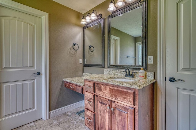 bathroom with a textured wall, baseboards, and vanity