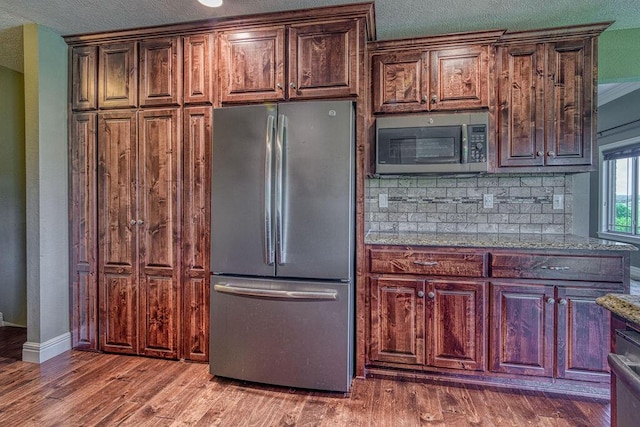 kitchen featuring light stone counters, backsplash, appliances with stainless steel finishes, wood finished floors, and baseboards