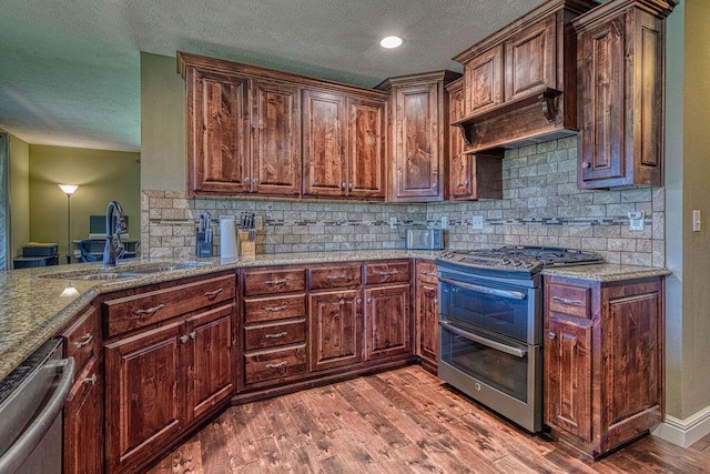 kitchen with light stone counters, stainless steel appliances, wood finished floors, a sink, and backsplash