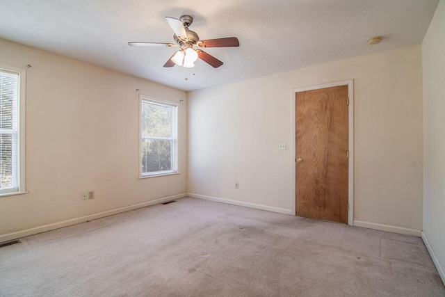 unfurnished room with light carpet, a ceiling fan, visible vents, and baseboards