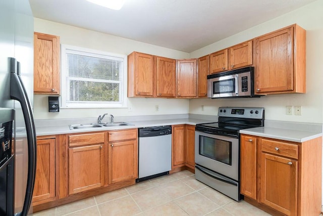 kitchen featuring brown cabinets, light tile patterned floors, light countertops, appliances with stainless steel finishes, and a sink