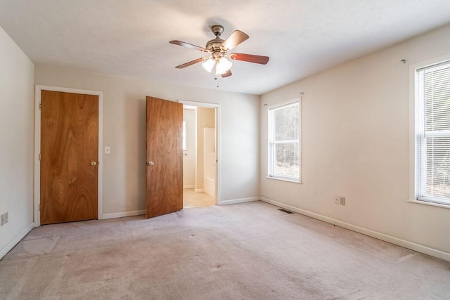 unfurnished bedroom featuring light carpet, ensuite bath, multiple windows, and baseboards