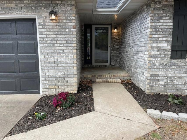 view of exterior entry with a garage, a shingled roof, and brick siding