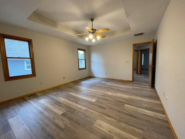 unfurnished room with a tray ceiling, visible vents, baseboards, and wood finished floors