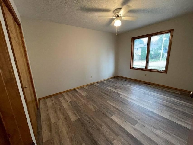 spare room with a textured ceiling, wood finished floors, and baseboards