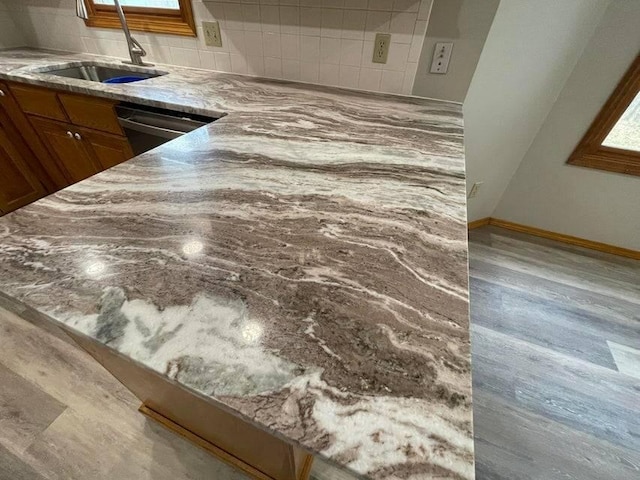 details featuring baseboards, brown cabinets, wood finished floors, a sink, and backsplash