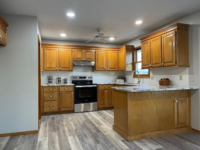 kitchen with a peninsula, brown cabinetry, electric range, and light countertops