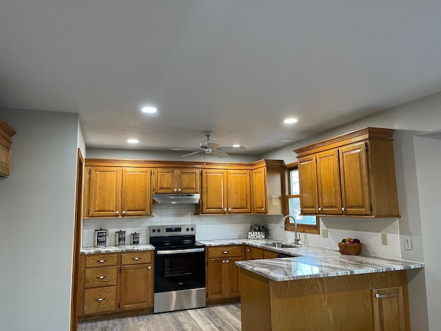 kitchen with electric stove, brown cabinets, a peninsula, under cabinet range hood, and a sink