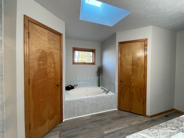 full bath featuring a textured ceiling, a garden tub, a skylight, wood finished floors, and baseboards