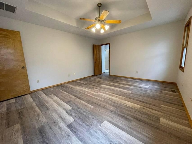 empty room with wood finished floors, a raised ceiling, visible vents, and baseboards