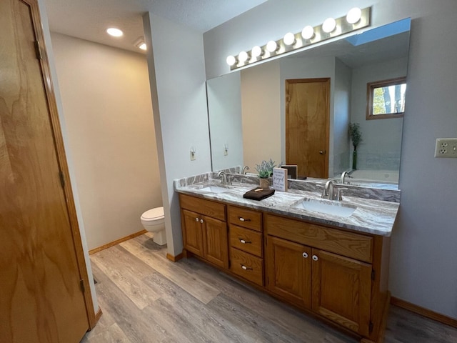 bathroom with double vanity, wood finished floors, a sink, and baseboards